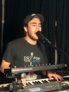 Michael Smedley standing behind a musical keyboard singing into a microphone